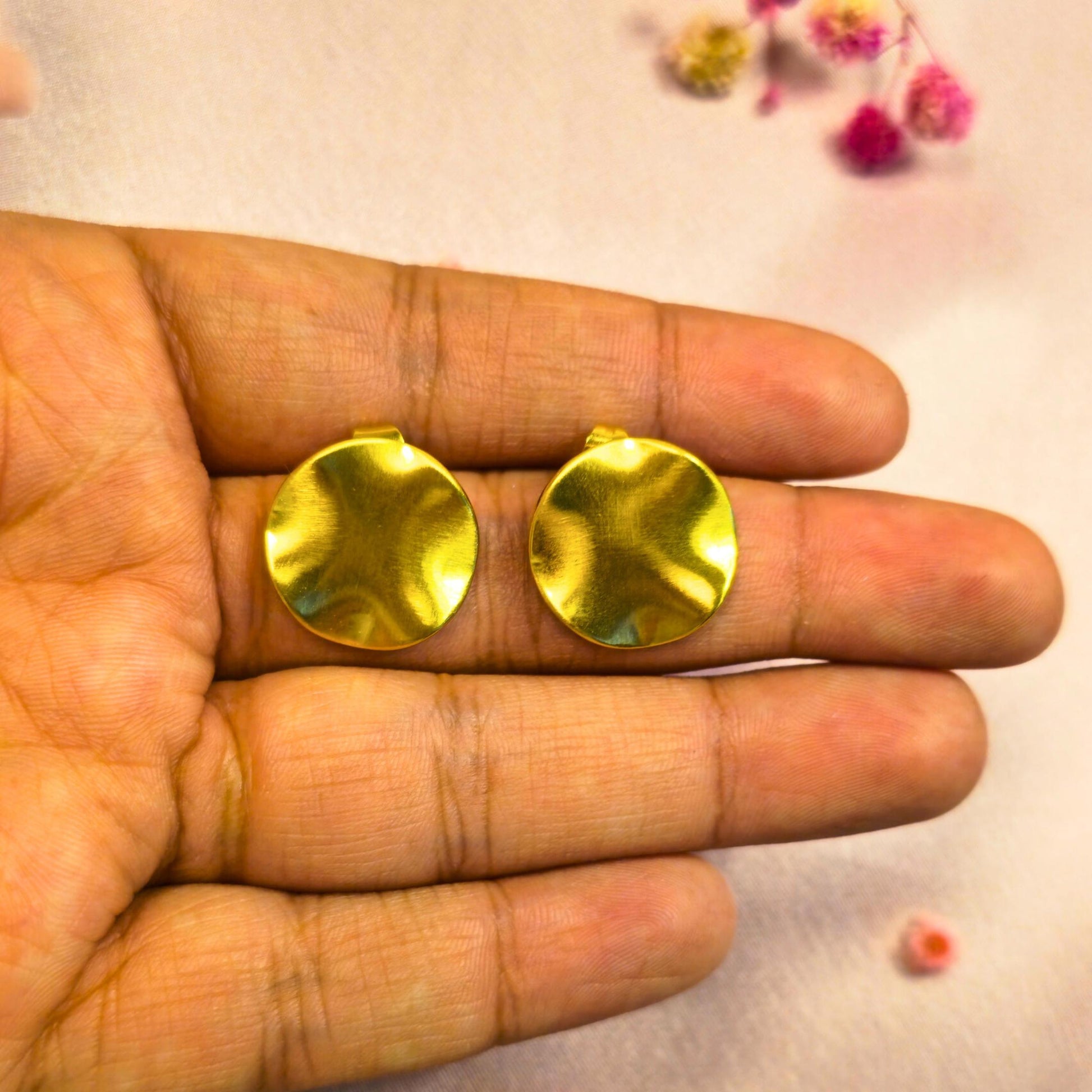 Gold round earrings held between fingers against a light background