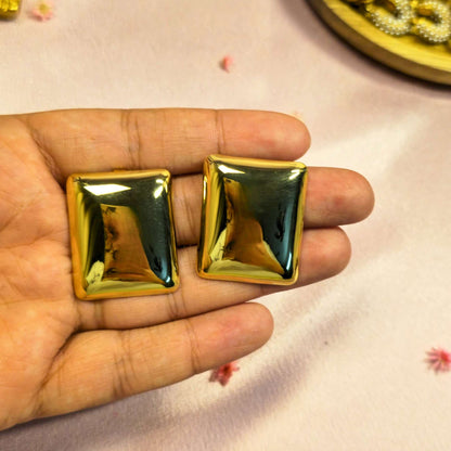 Gold square-shaped stud earring held in a hand on a light pink background