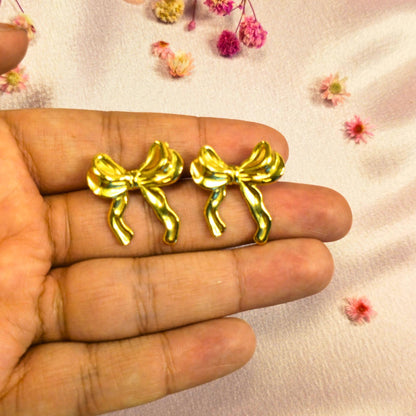 Gold bow-shaped earrings held between fingers with a light background