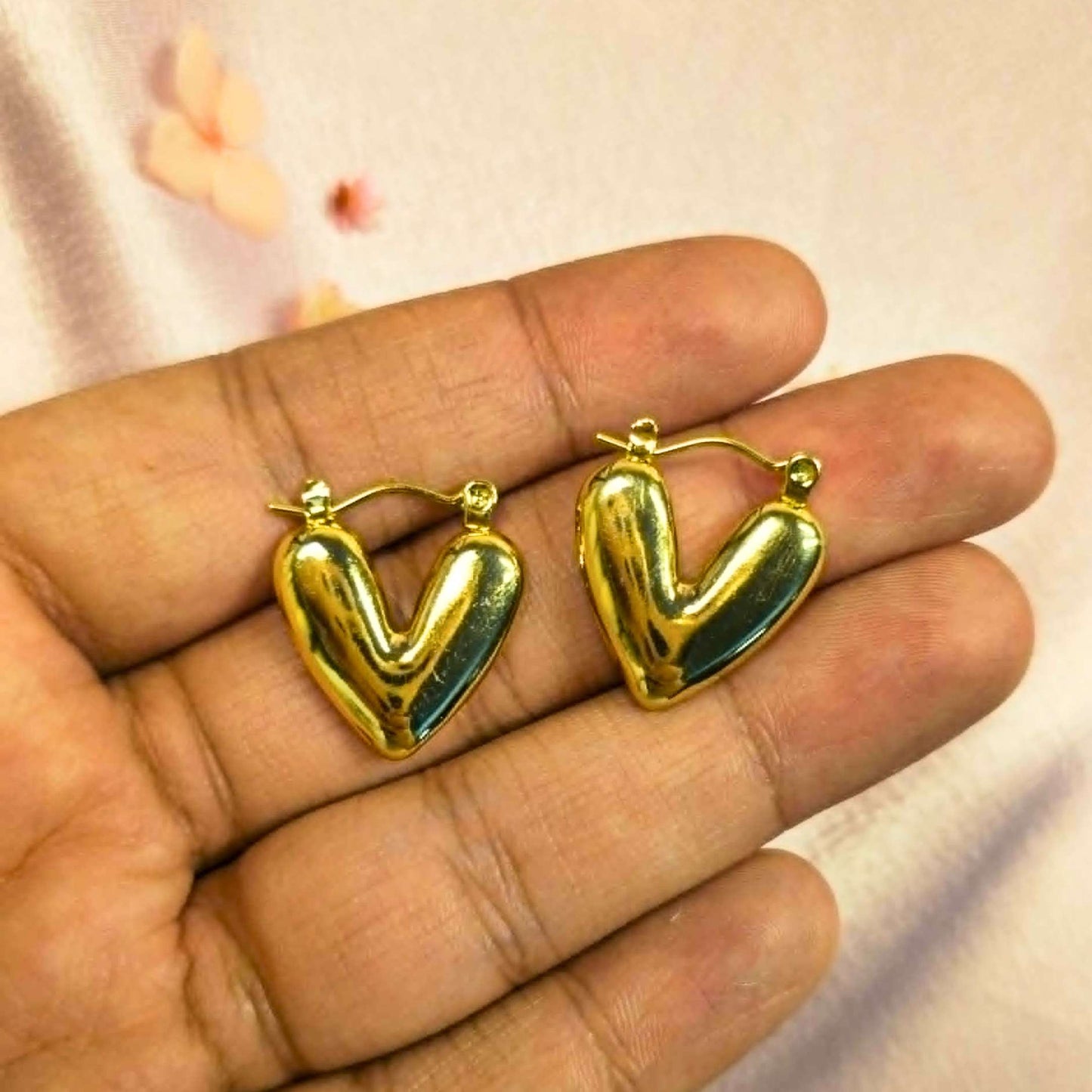 Gold heart-shaped earrings held between fingers against a light background