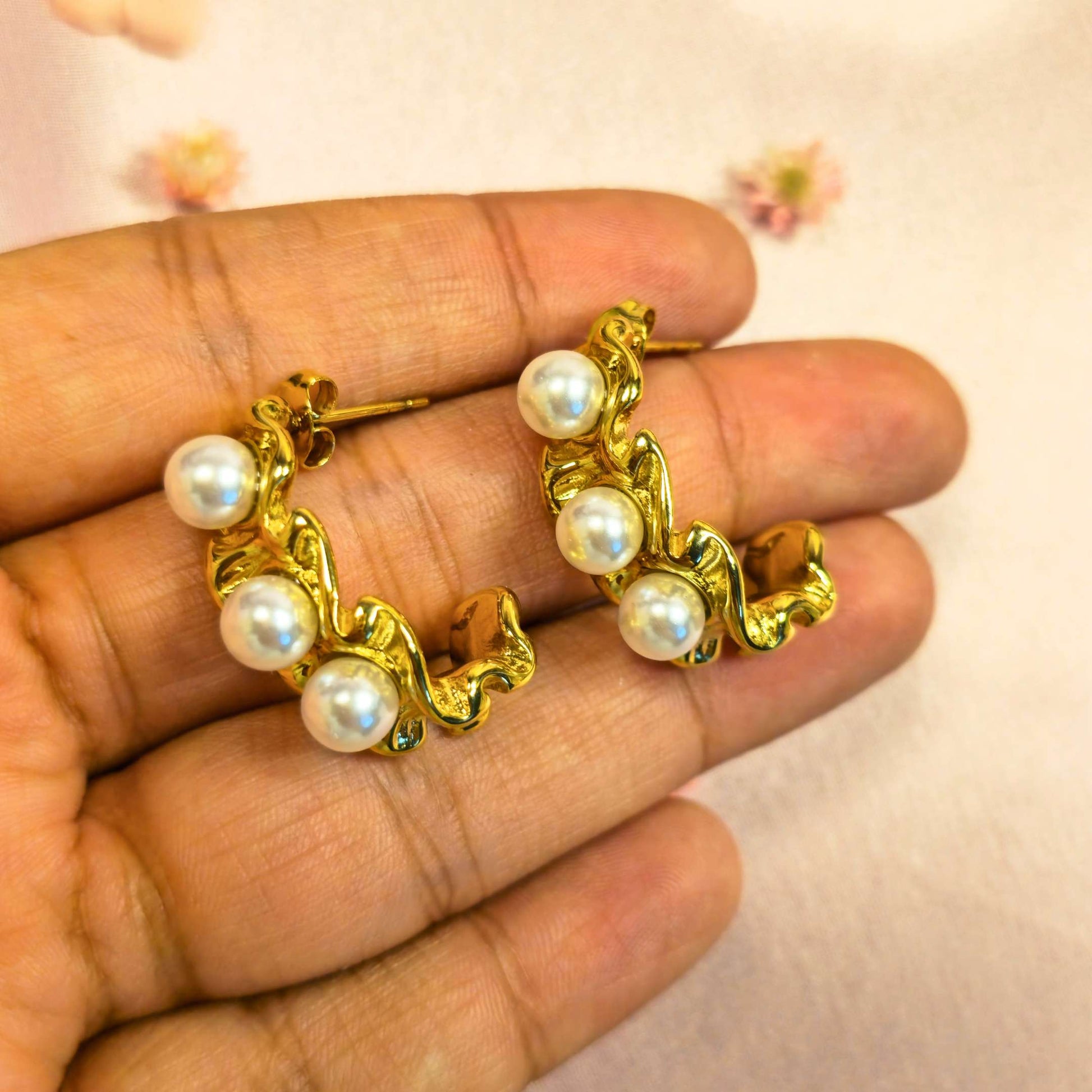 Gold hoop earrings with pearls held in a hand against a light background