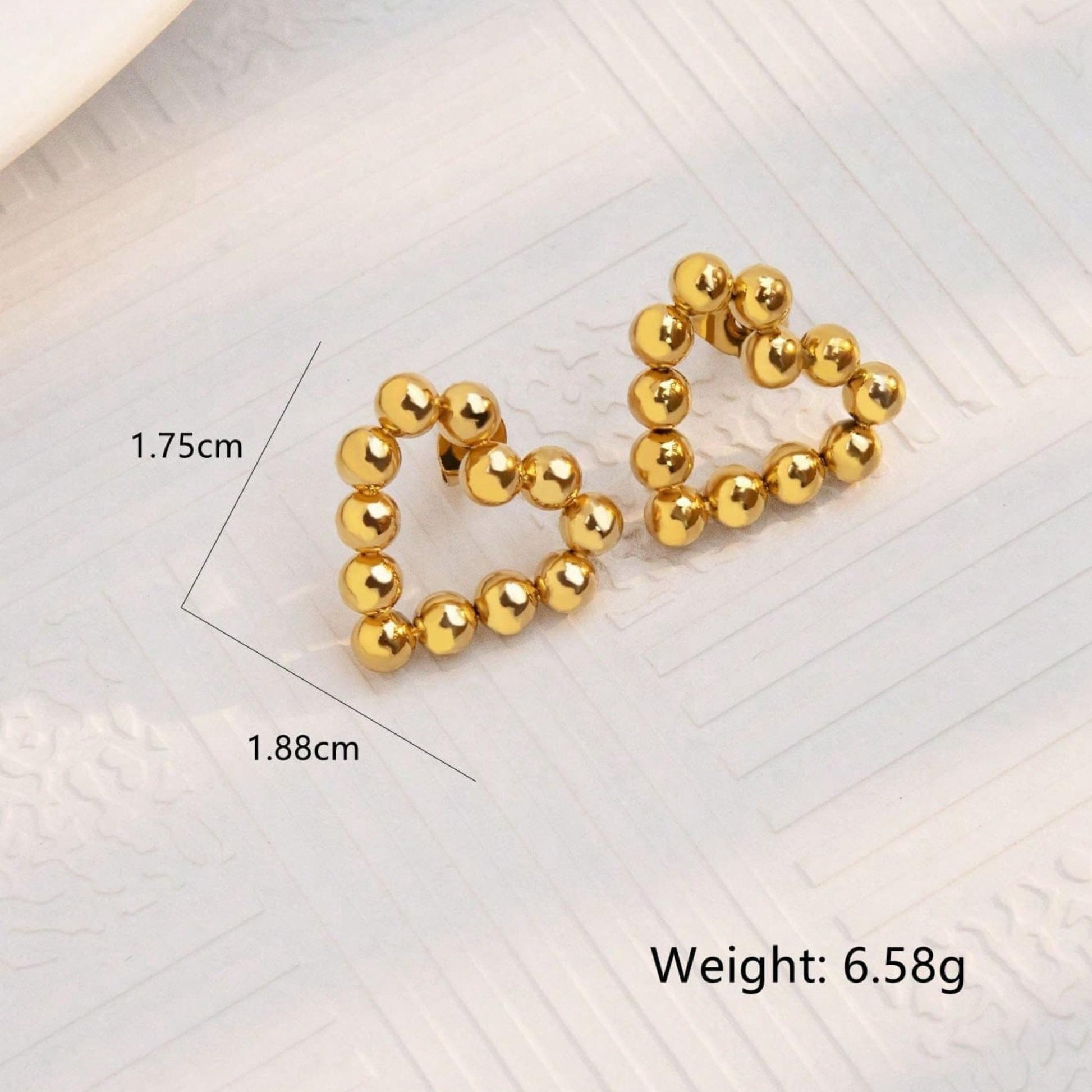 Gold heart-shaped earrings with measurements and weight on a light background