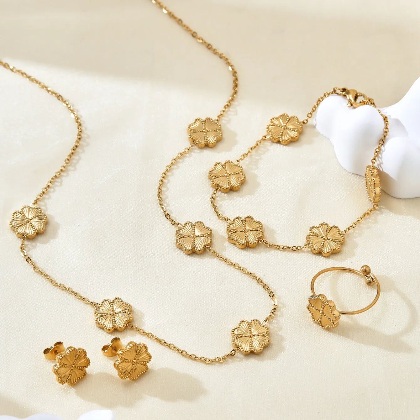 Gold necklace, bracelet, ring, and earrings on a beige surface