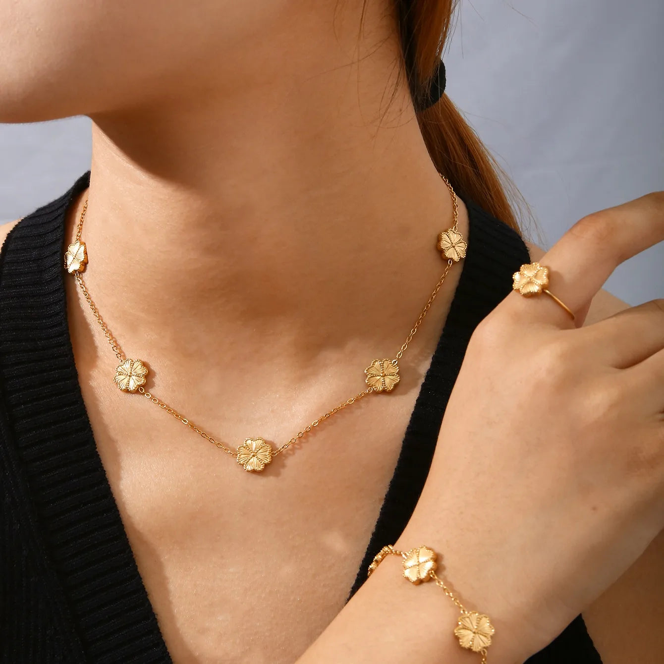Gold necklace, ring, and bracelet on a person against a neutral background