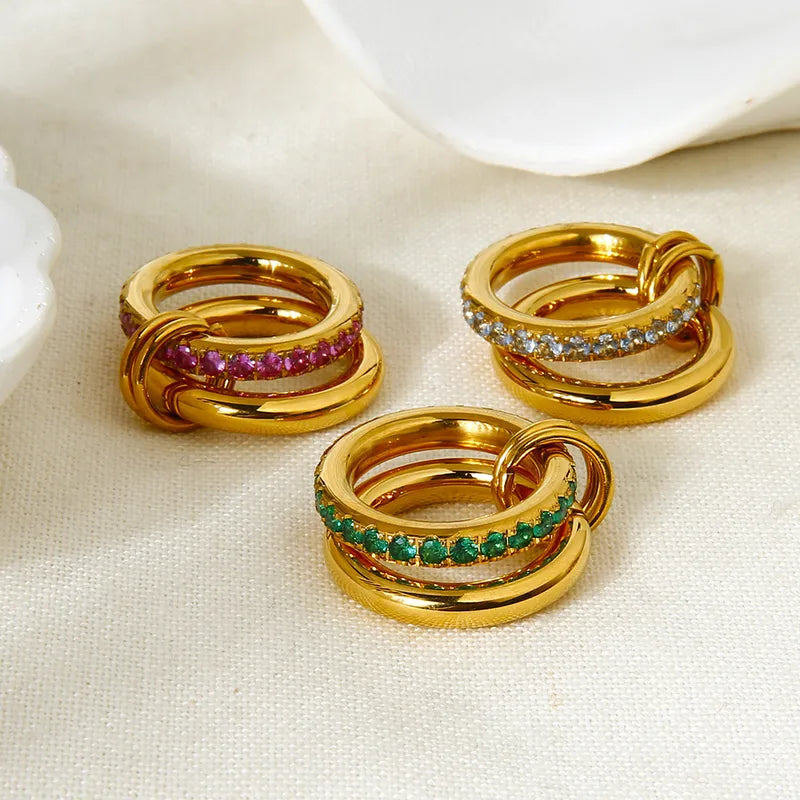 Three gold rings with gemstones on a beige surface