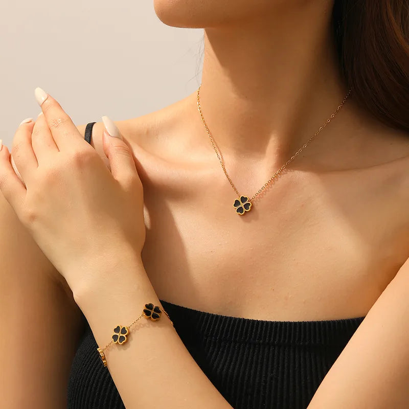 Woman wearing a gold necklace and bracelet with clover pendants on a neutral background
