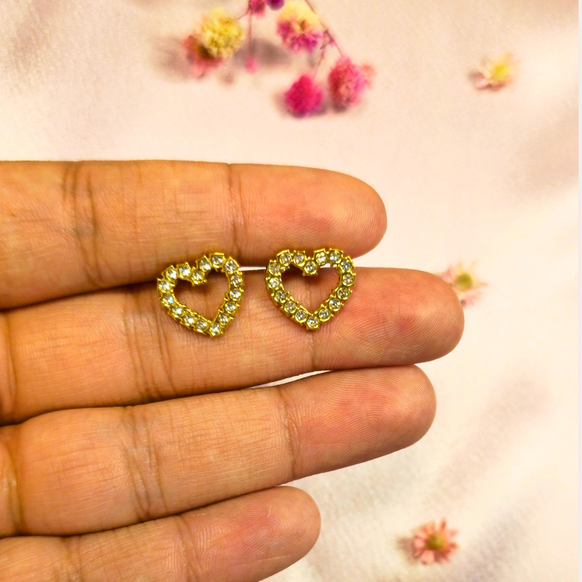 Heart-shaped earrings with clear gemstones held between fingers with a soft floral background