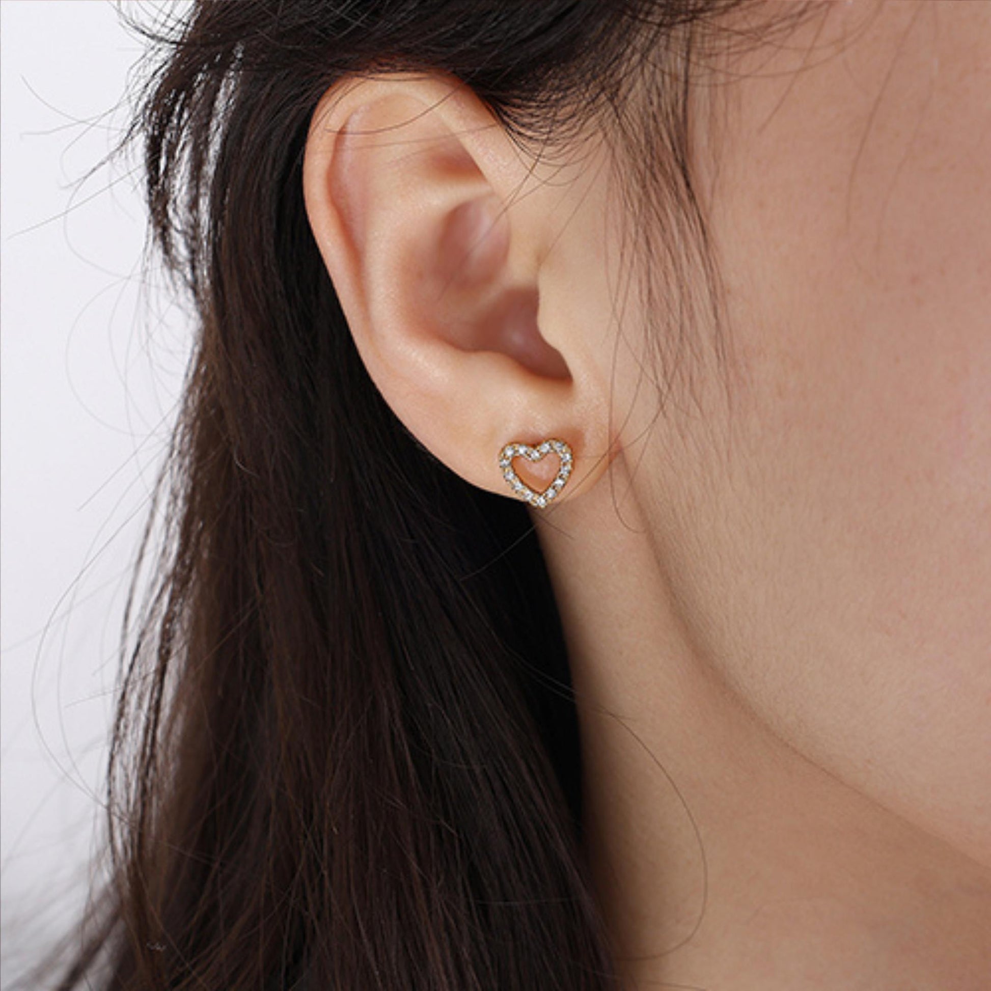 Heart-shaped clear gemstone earring worn by a person with dark hair.