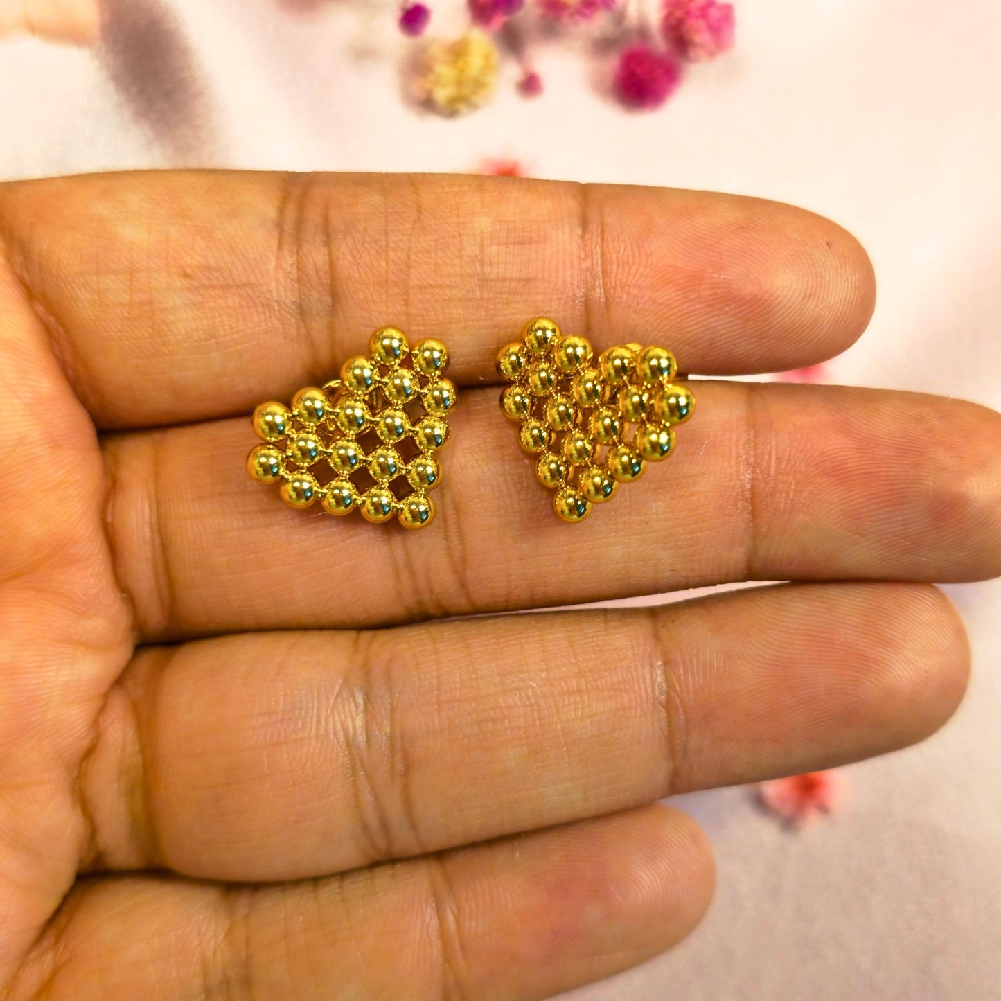 Gold heart-shaped beaded earrings held between fingers with a blurred background