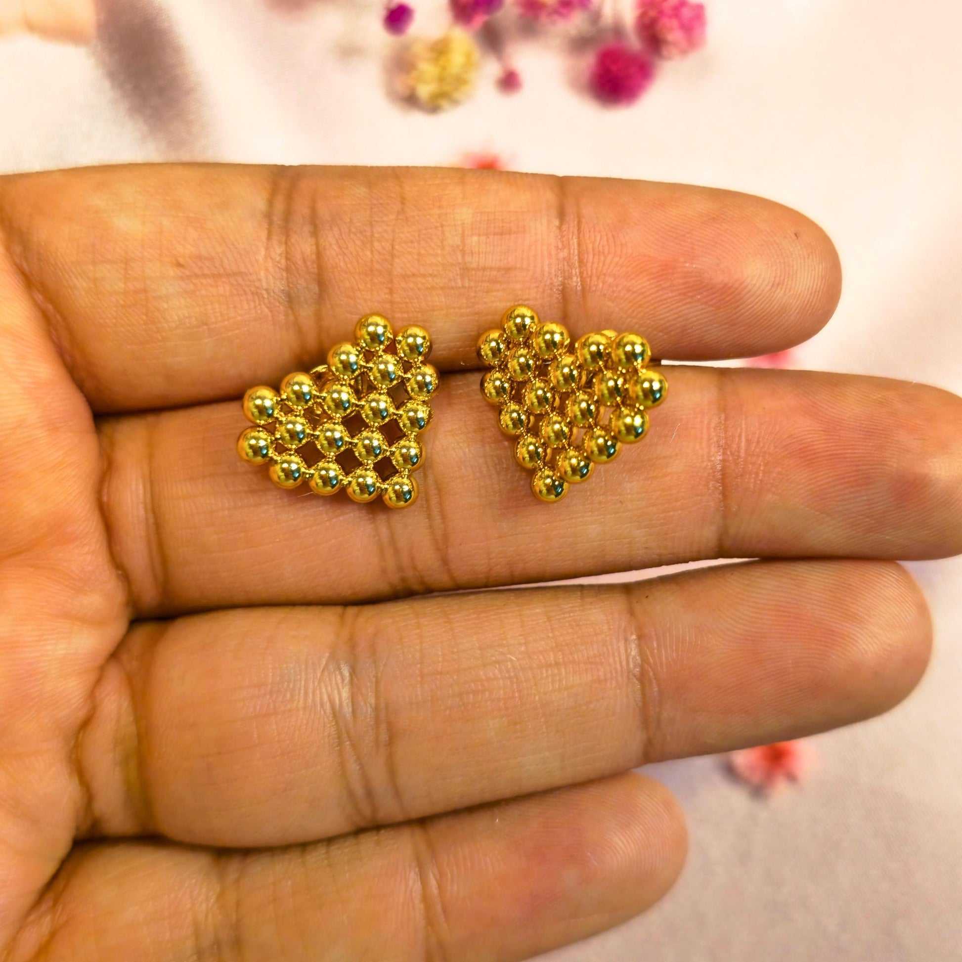 Gold heart-shaped beaded earrings held between fingers with a blurred background
