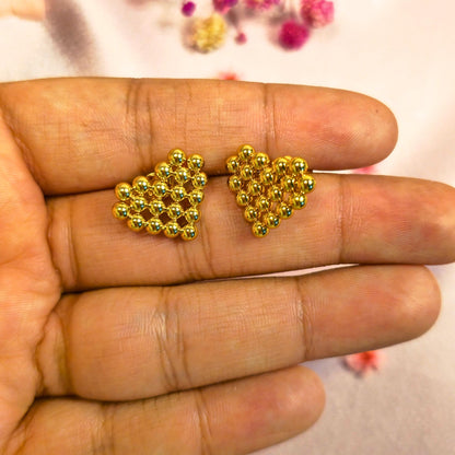 Gold heart-shaped beaded earrings held between fingers with a blurred background