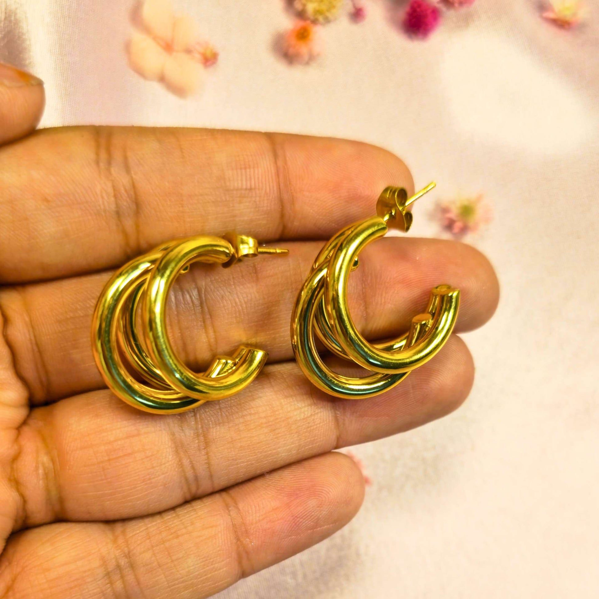 Gold hoop earrings held between fingers against a floral-patterned background