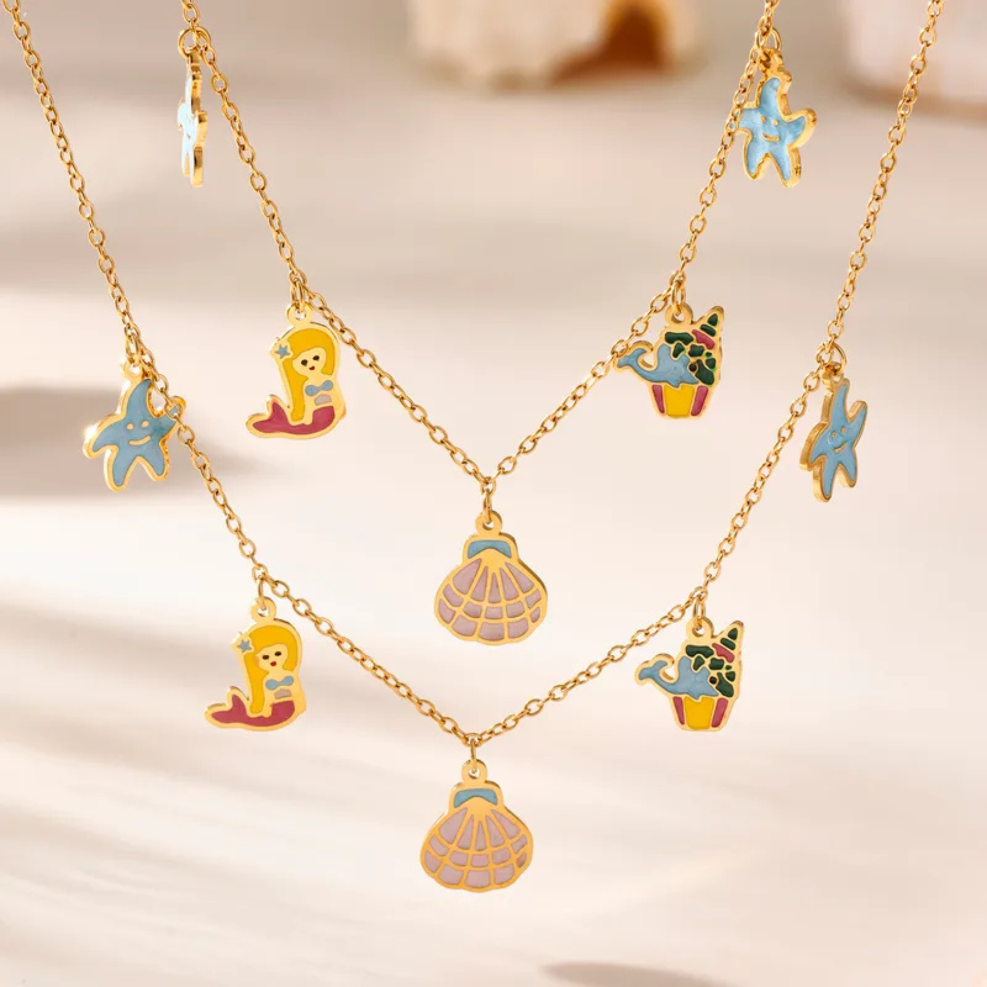 Gold necklaces with colorful sea-themed charms on a beige background