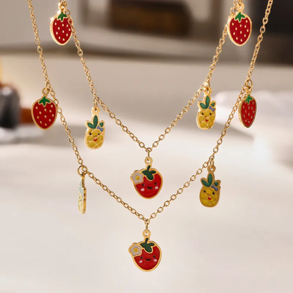 Gold necklace with strawberry and pineapple pendants on a light background