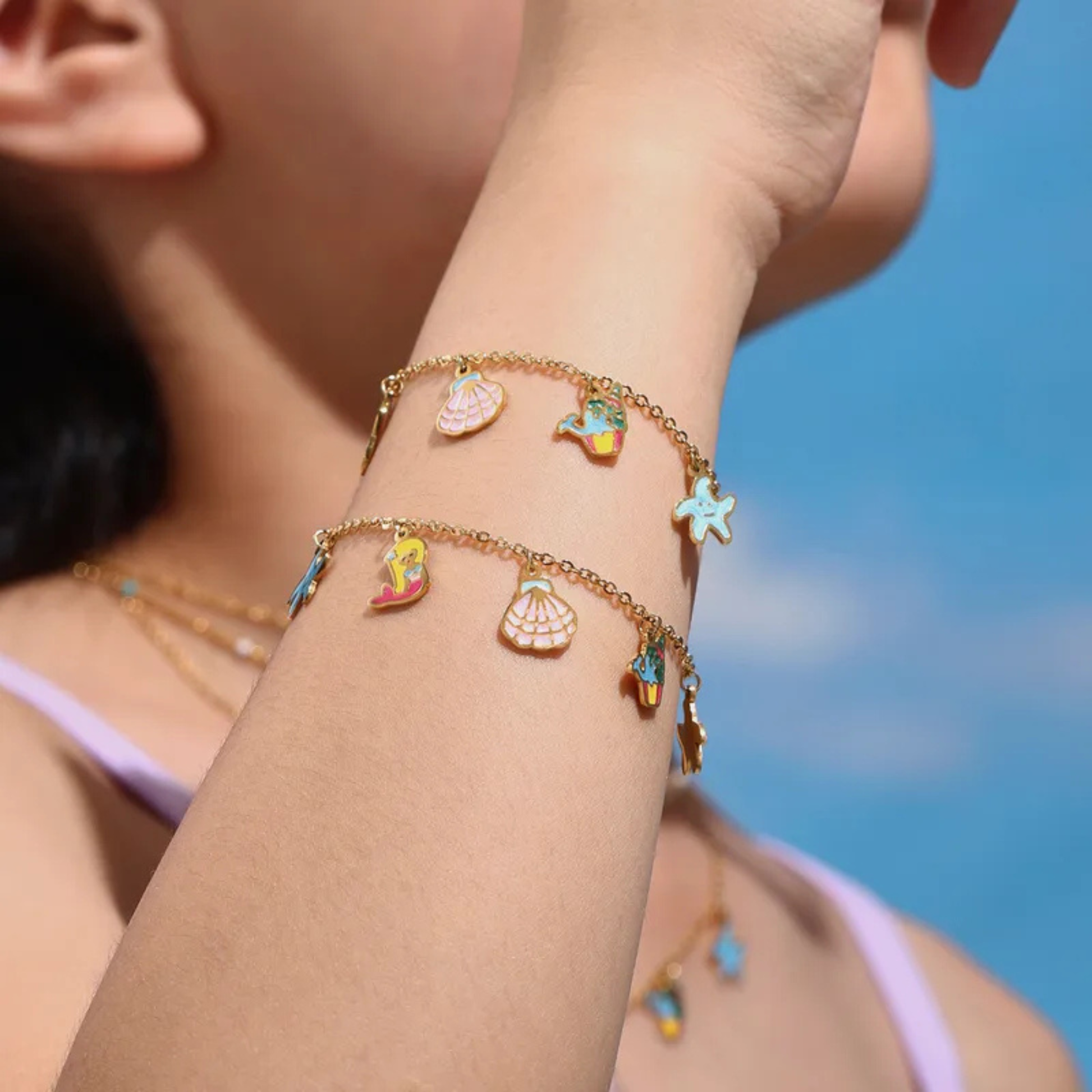 Close-up of a person's arm wearing a gold bracelet with colorful charms against a blue sky.