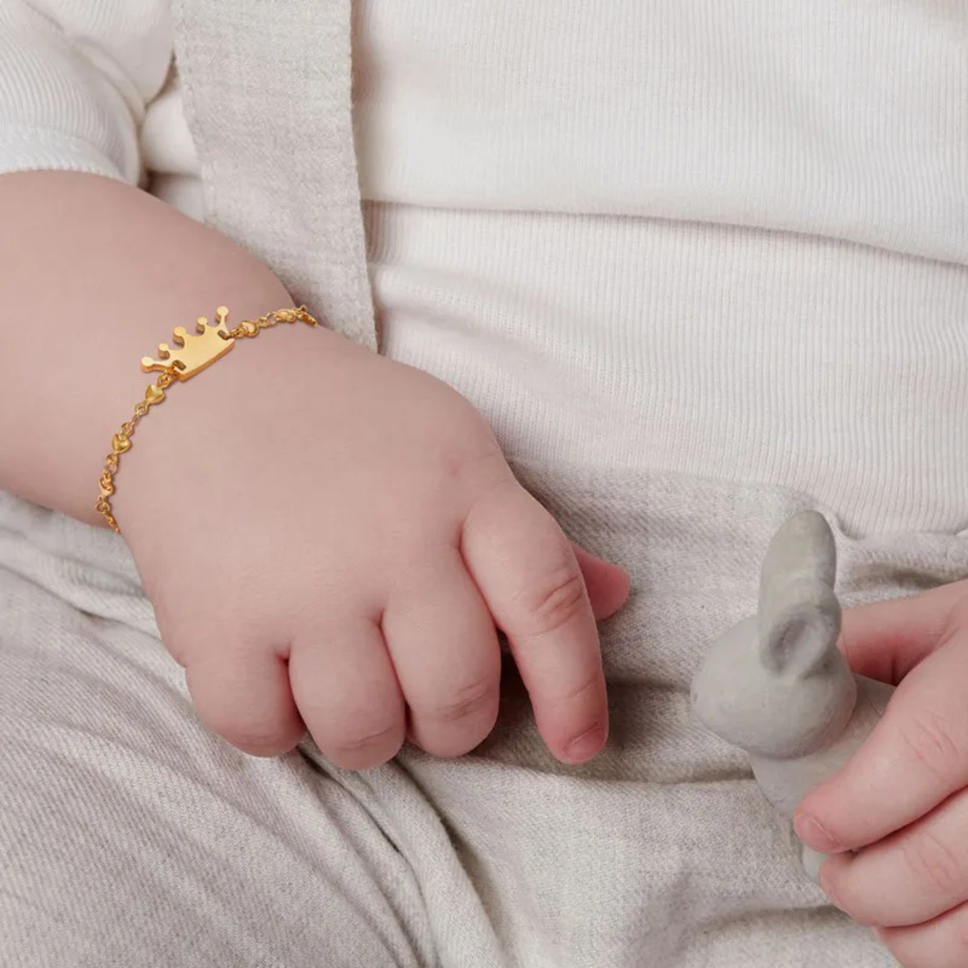 Child's hand wearing a gold bracelet holding a gray toy