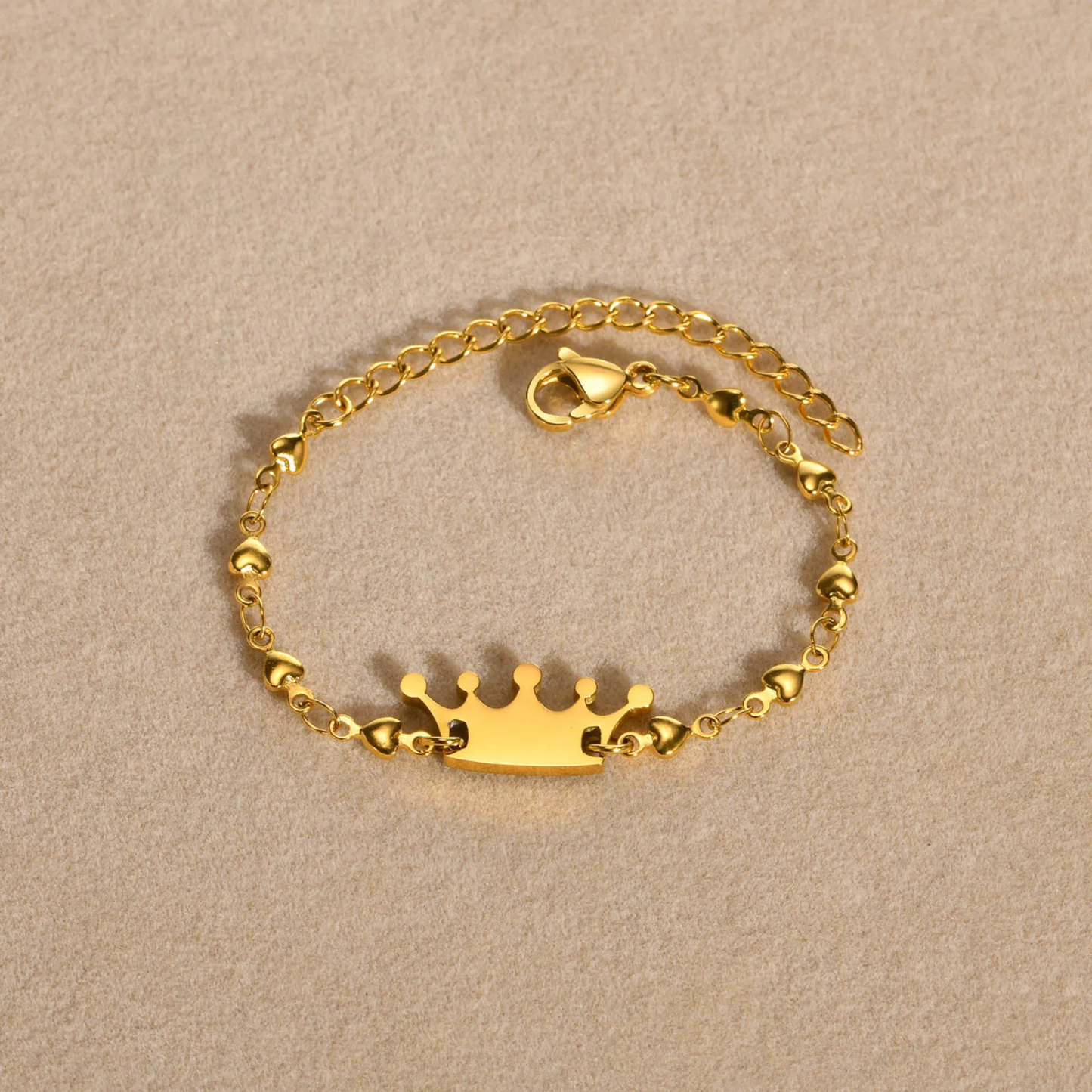 Gold bracelet with a crown charm on a beige background