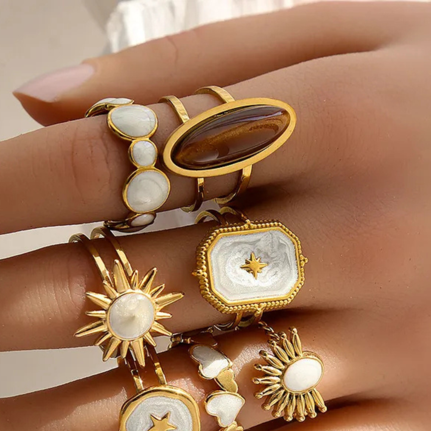 Gold and stone rings on a hand against a neutral background