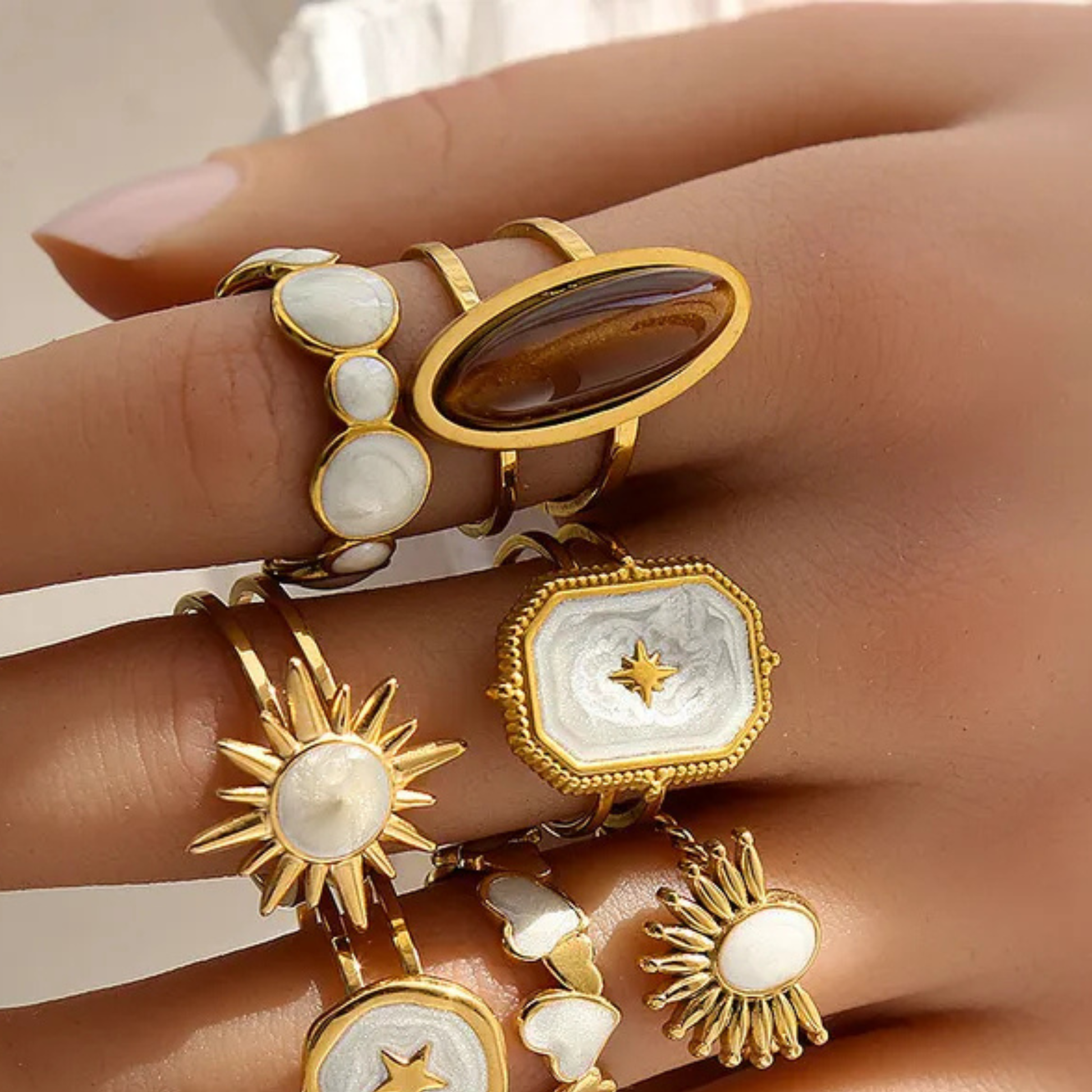 Gold and stone rings on a hand against a neutral background