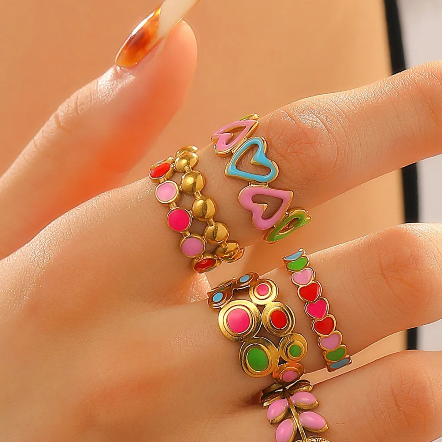Colorful heart-shaped rings on a hand against a neutral background