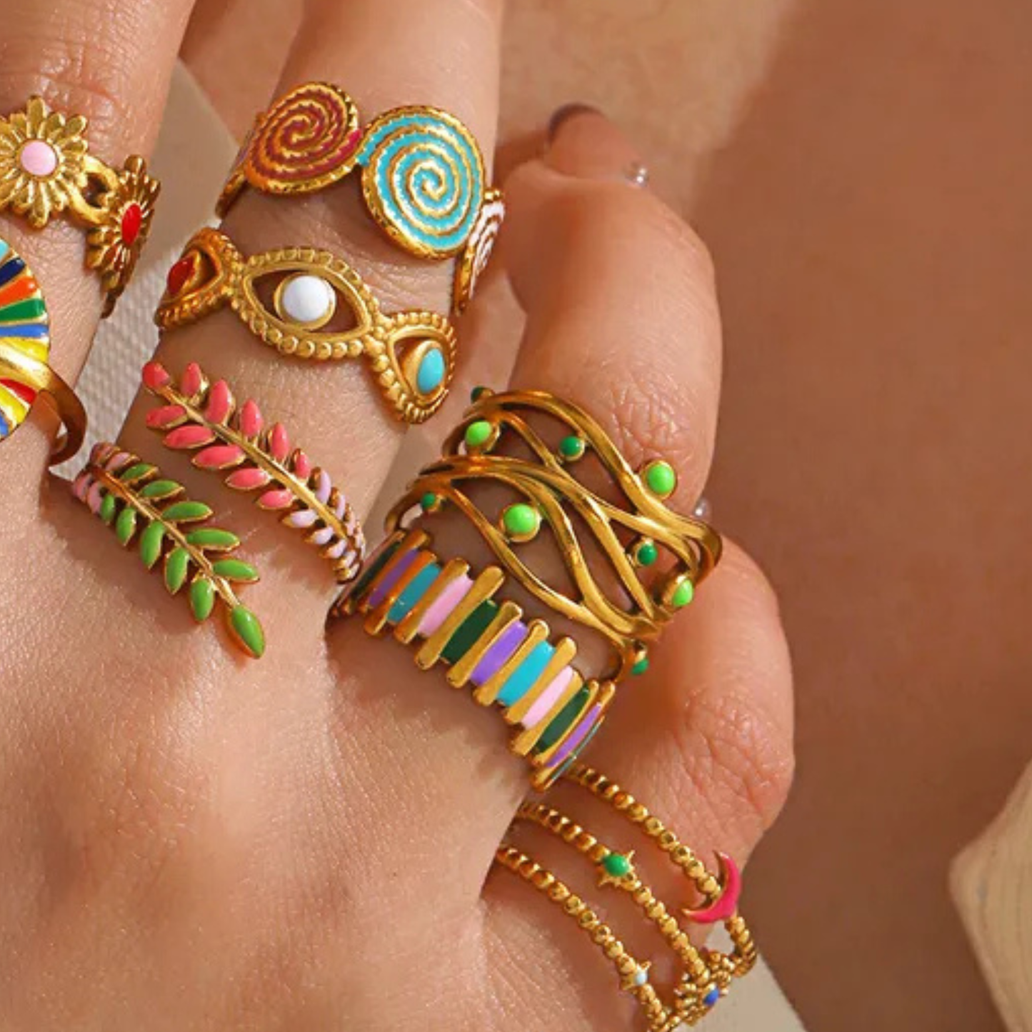 Close-up of a hand wearing multiple colorful rings on a neutral background