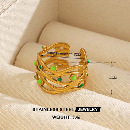 Gold ring with green stones on a beige fabric background, showing measurements and weight details.