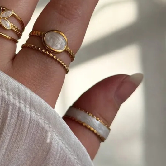 Close-up of a hand wearing multiple gold and white rings on a blurred background