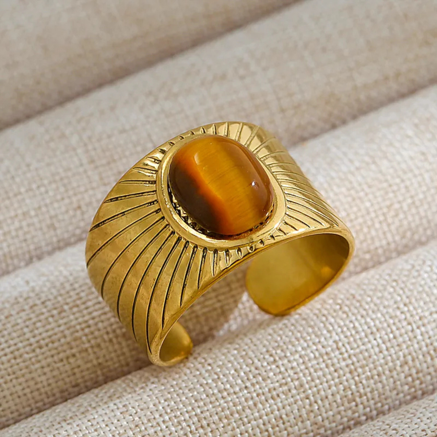 Gold bracelet with a central brown stone on a beige fabric background