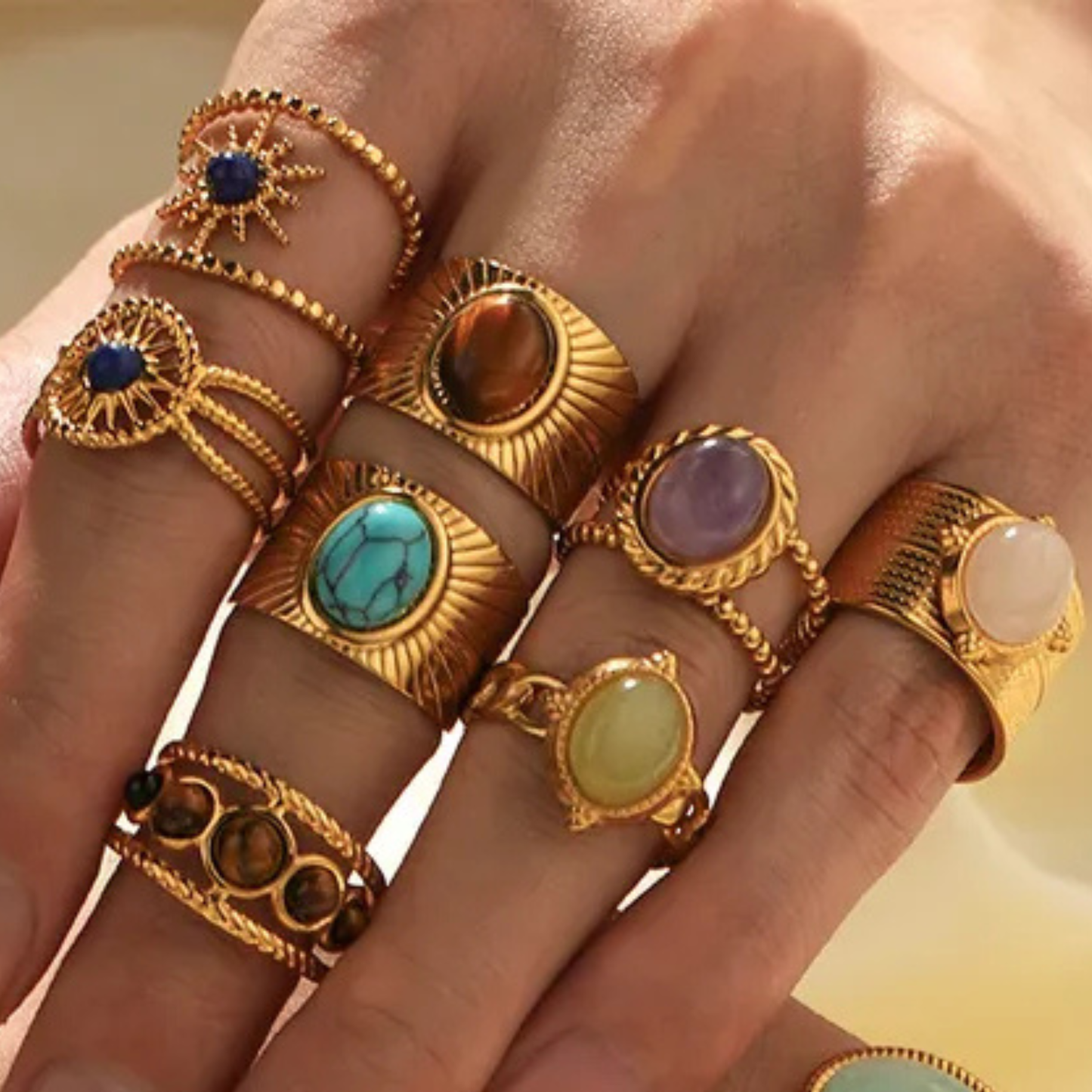 Hand wearing multiple gold rings with gemstones on a neutral background