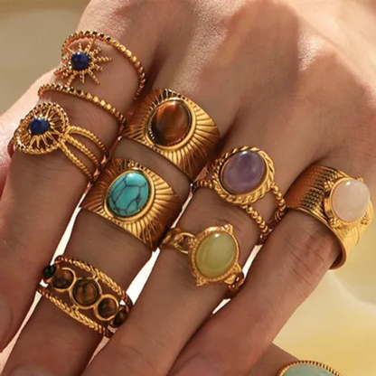 Hand wearing multiple gold rings with gemstones on a neutral background