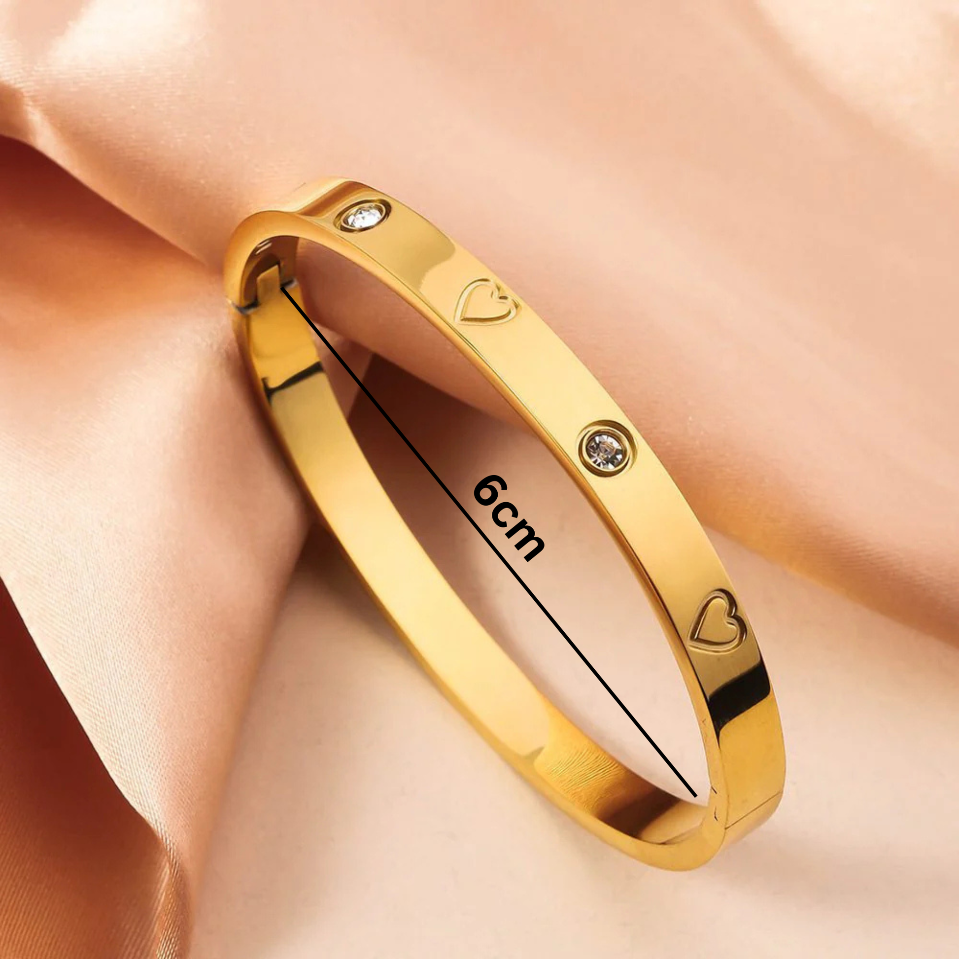 Gold bracelet with heart and diamond designs on a soft pink background