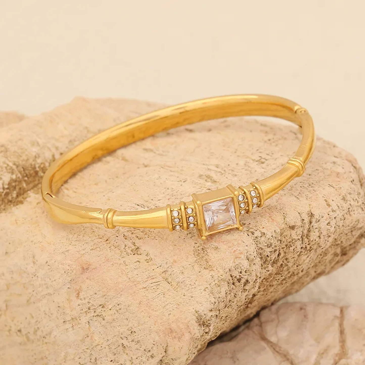 Gold bracelet with a central gemstone on a beige stone background