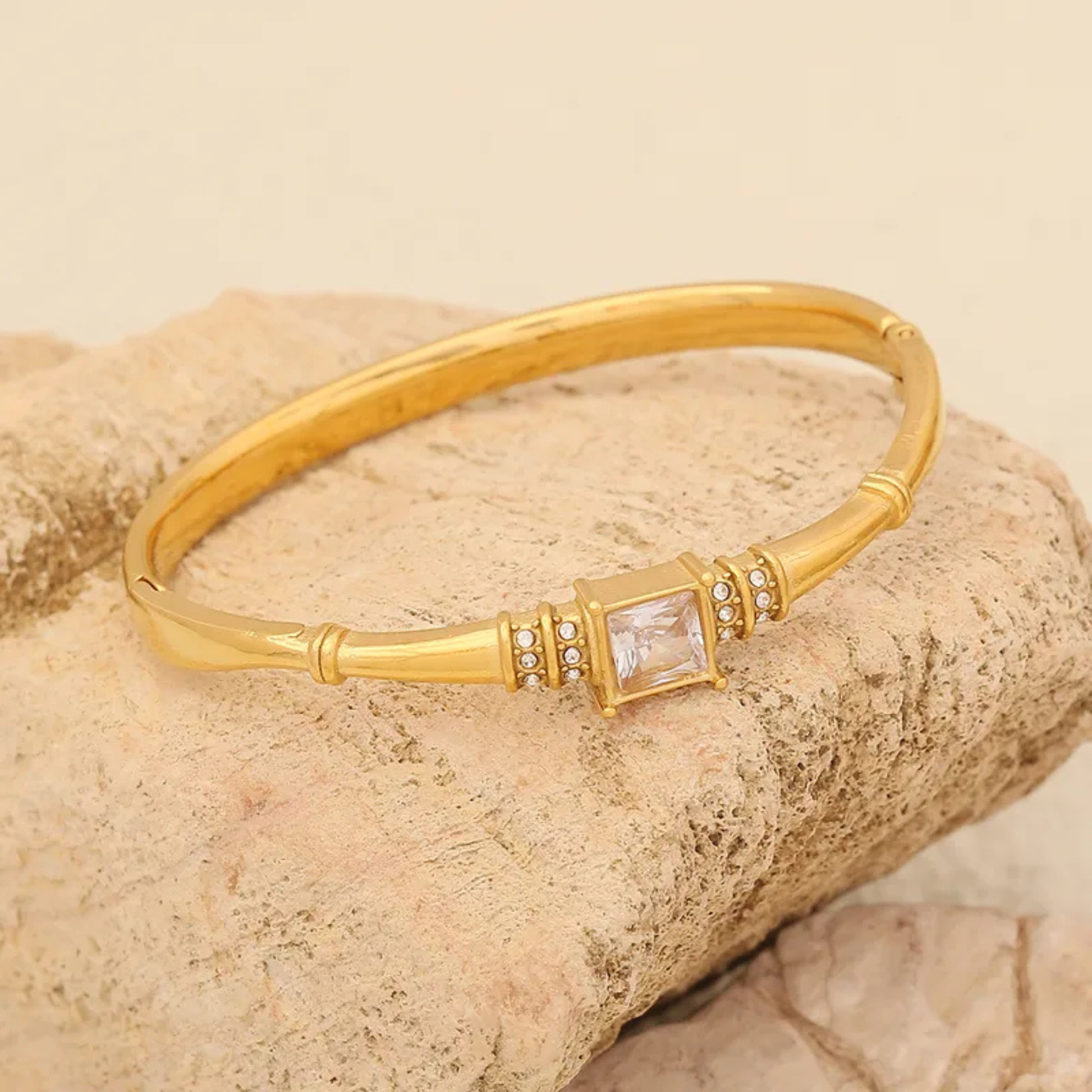 Gold bracelet with a central gemstone on a beige stone background