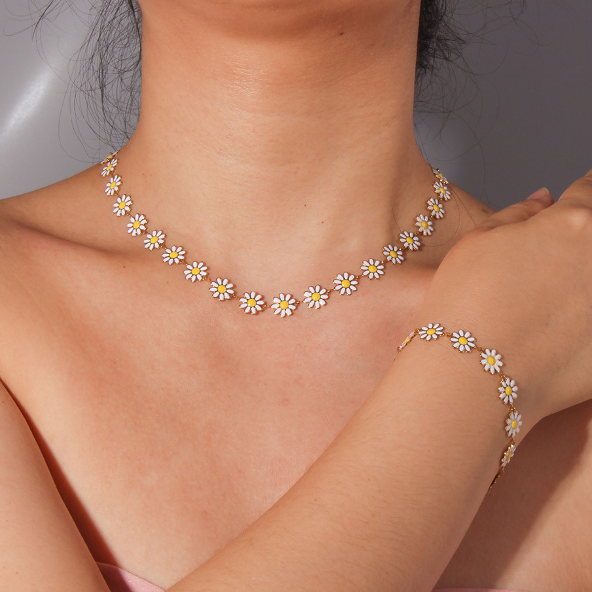Person wearing a daisy chain necklace and bracelet on a neutral background