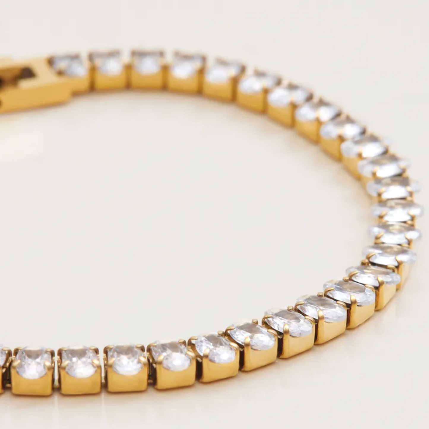 Gold bracelet with clear gemstones on a light background