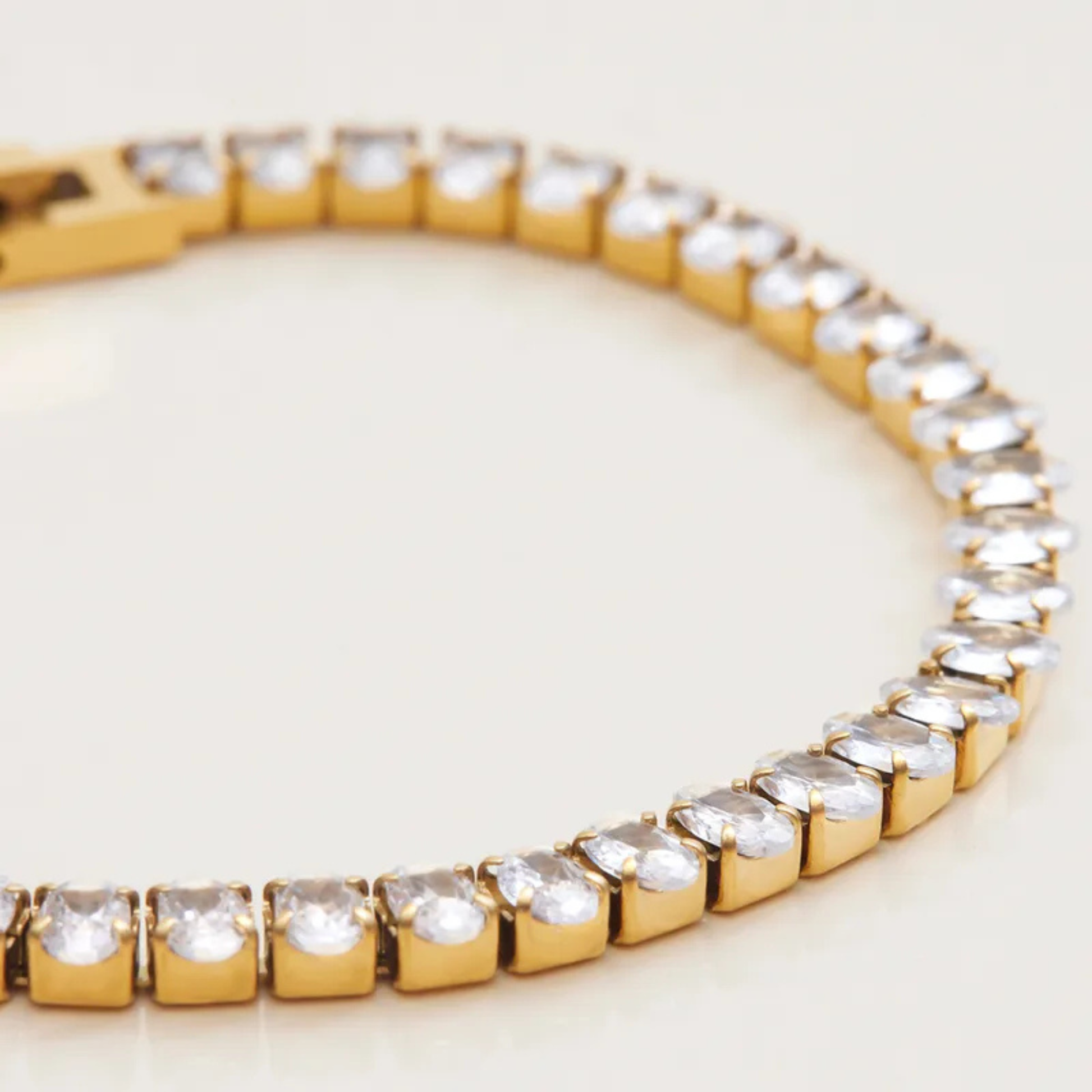Gold bracelet with clear gemstones on a light background