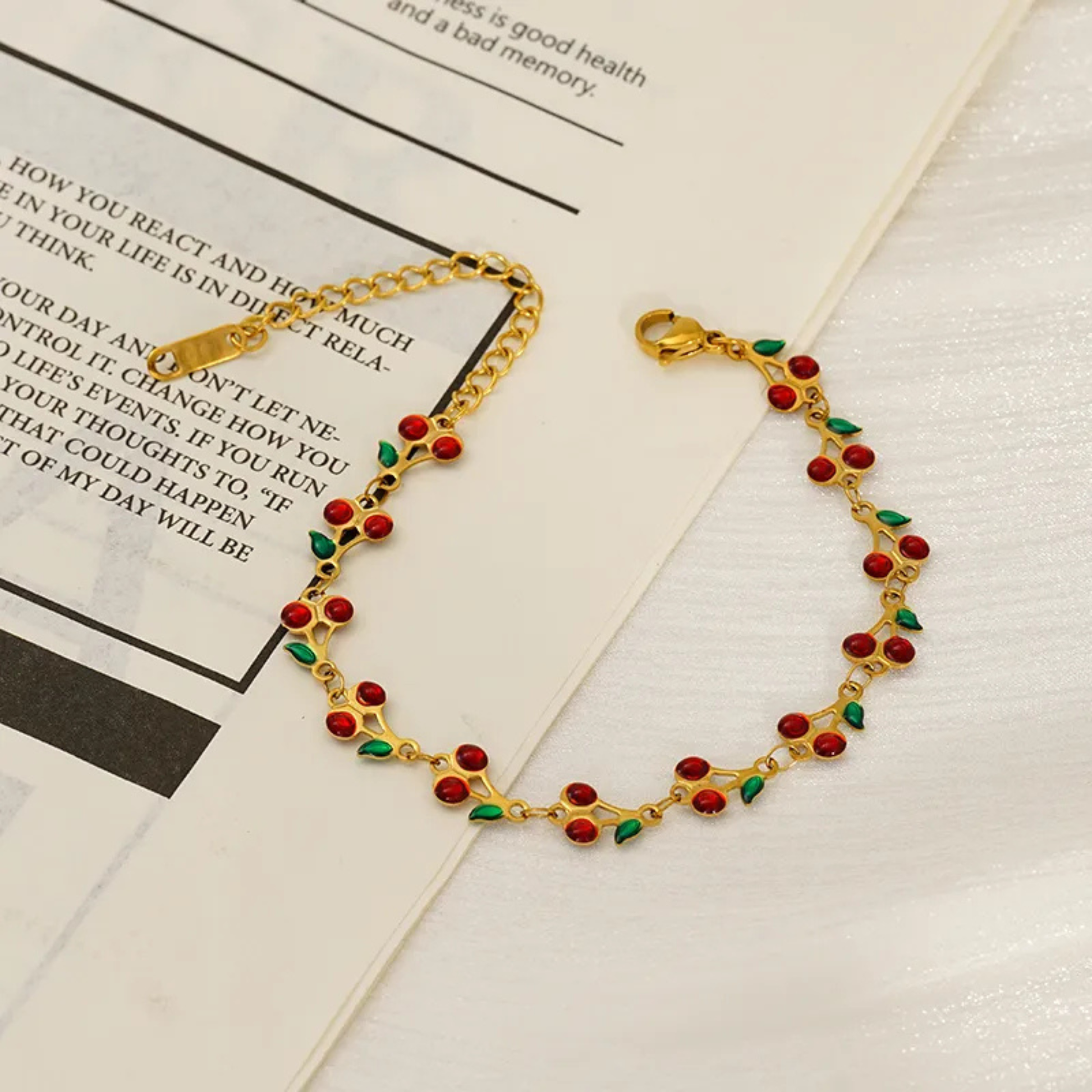 Gold bracelet with red cherry and green leaf beads on a newspaper background