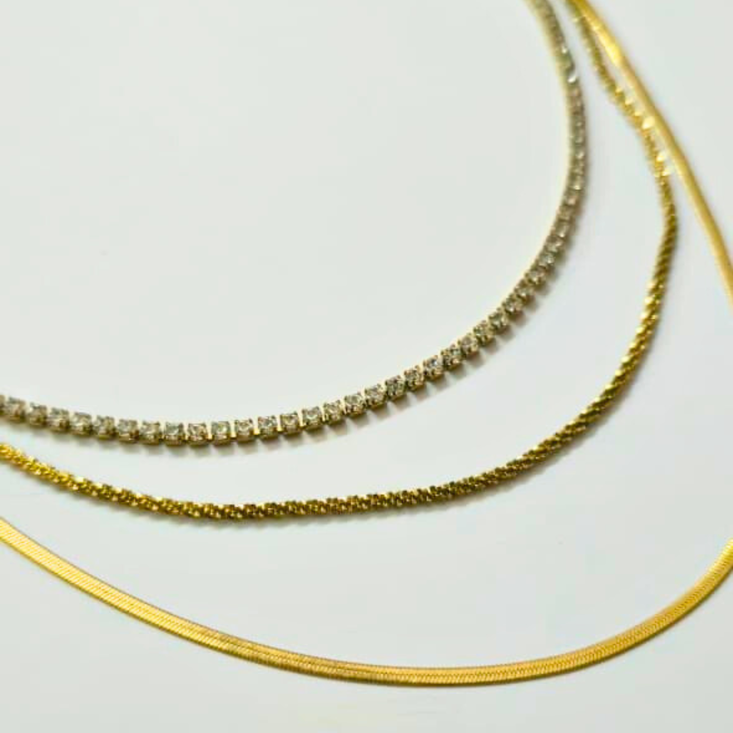 Three gold necklaces on a light gray background