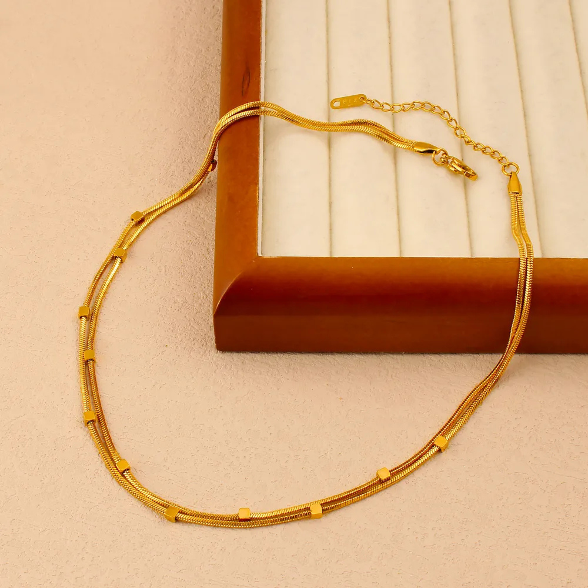 Gold necklace on a beige surface with a brown box in the background