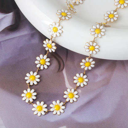 Daisy chain necklace with white flowers and yellow centers on a white plate against a purple fabric background.