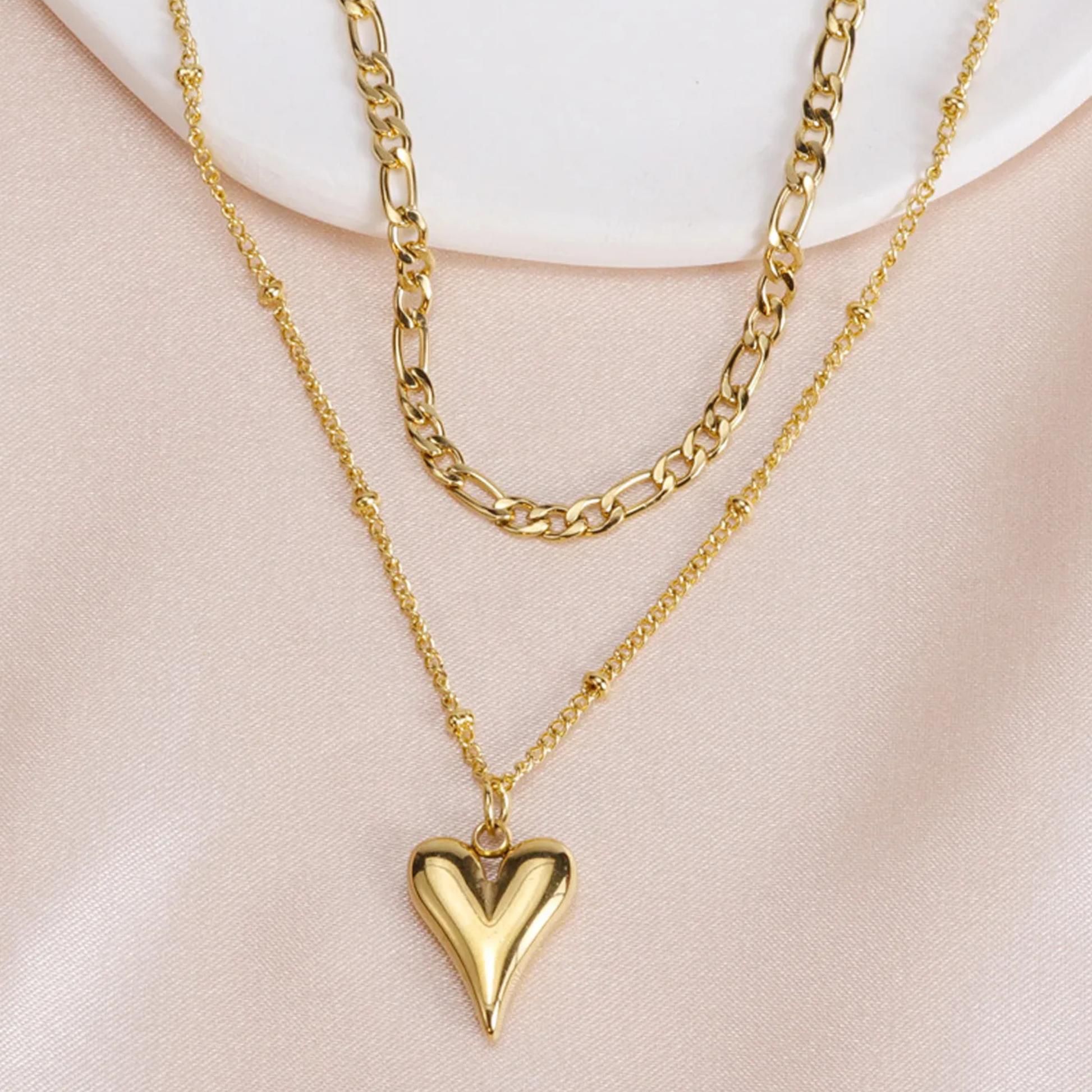 Gold heart pendant necklace on a person wearing a white top against a beige background