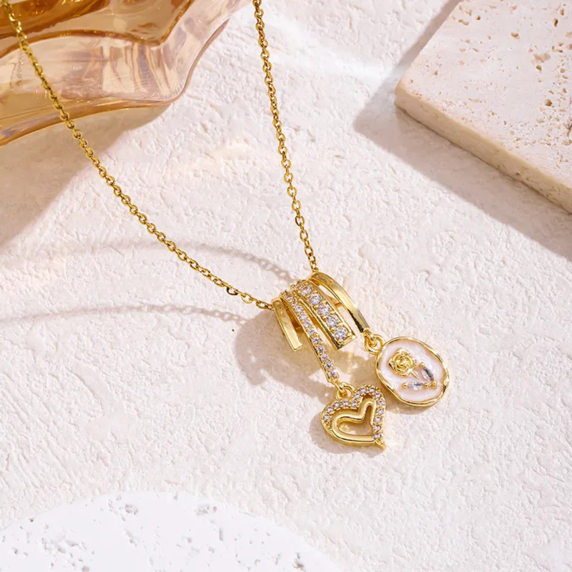 Gold necklace with heart and round pendants on a textured white surface