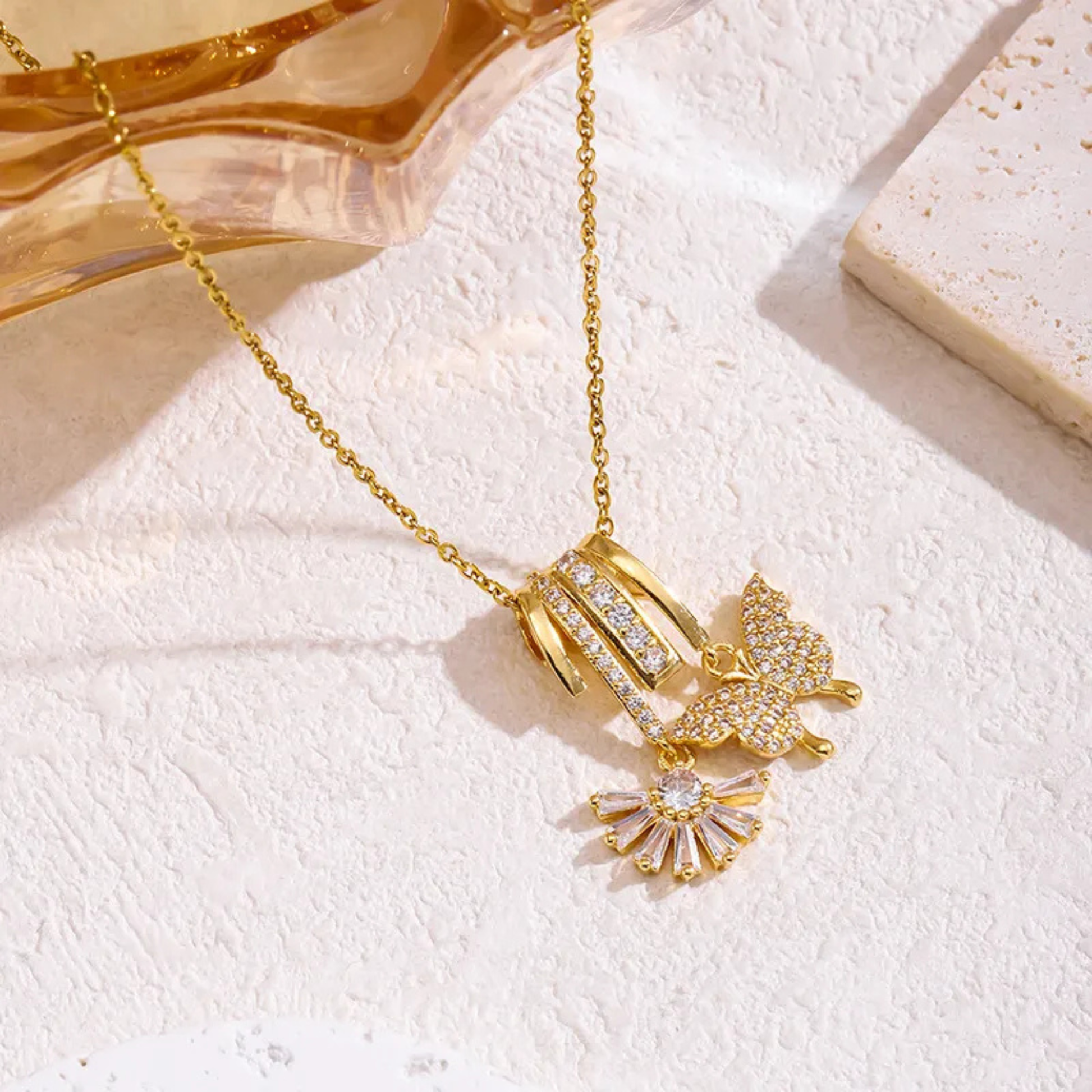 Gold necklace with butterfly and flower pendants on a textured white surface