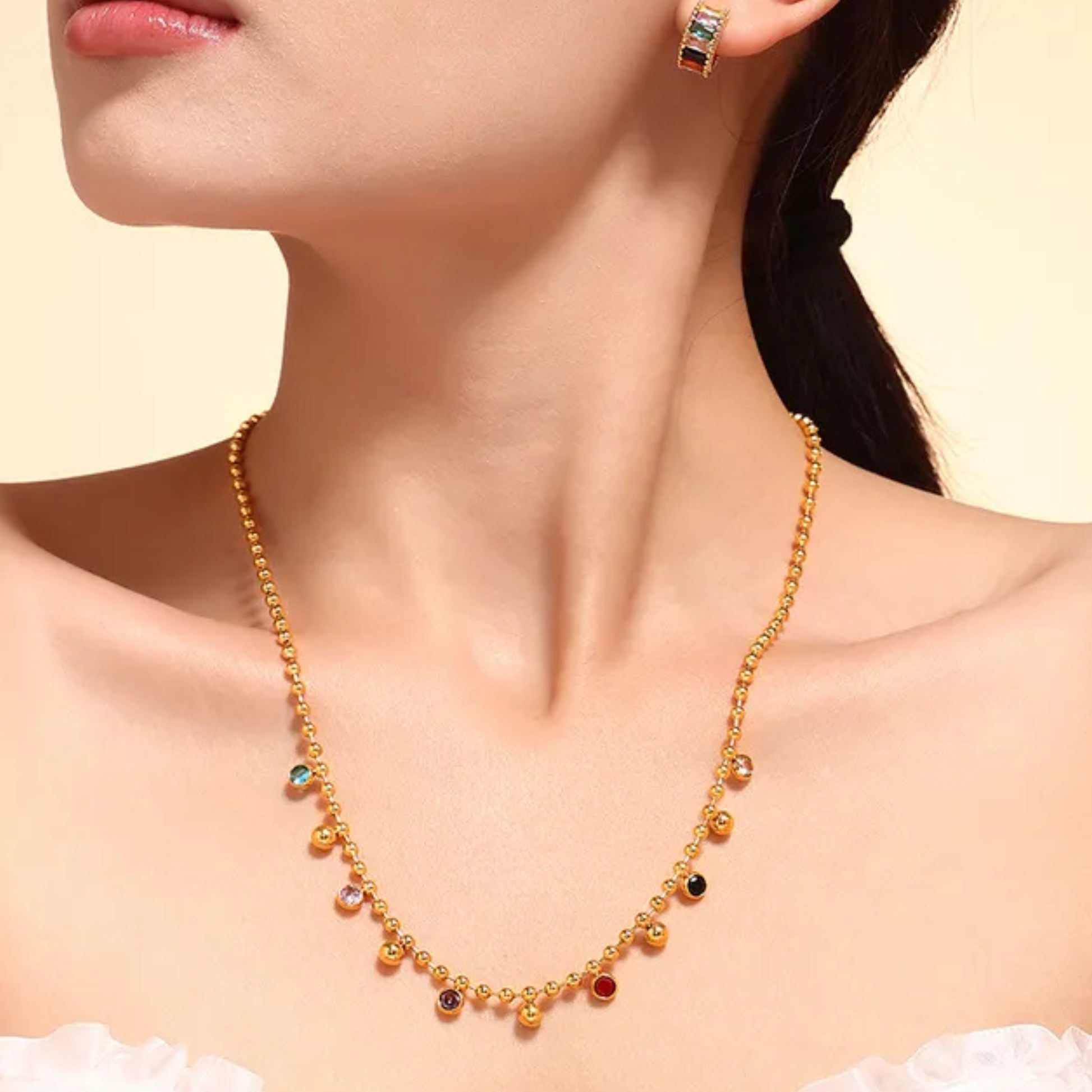 Gold necklace with colorful beads worn by a model on a beige background