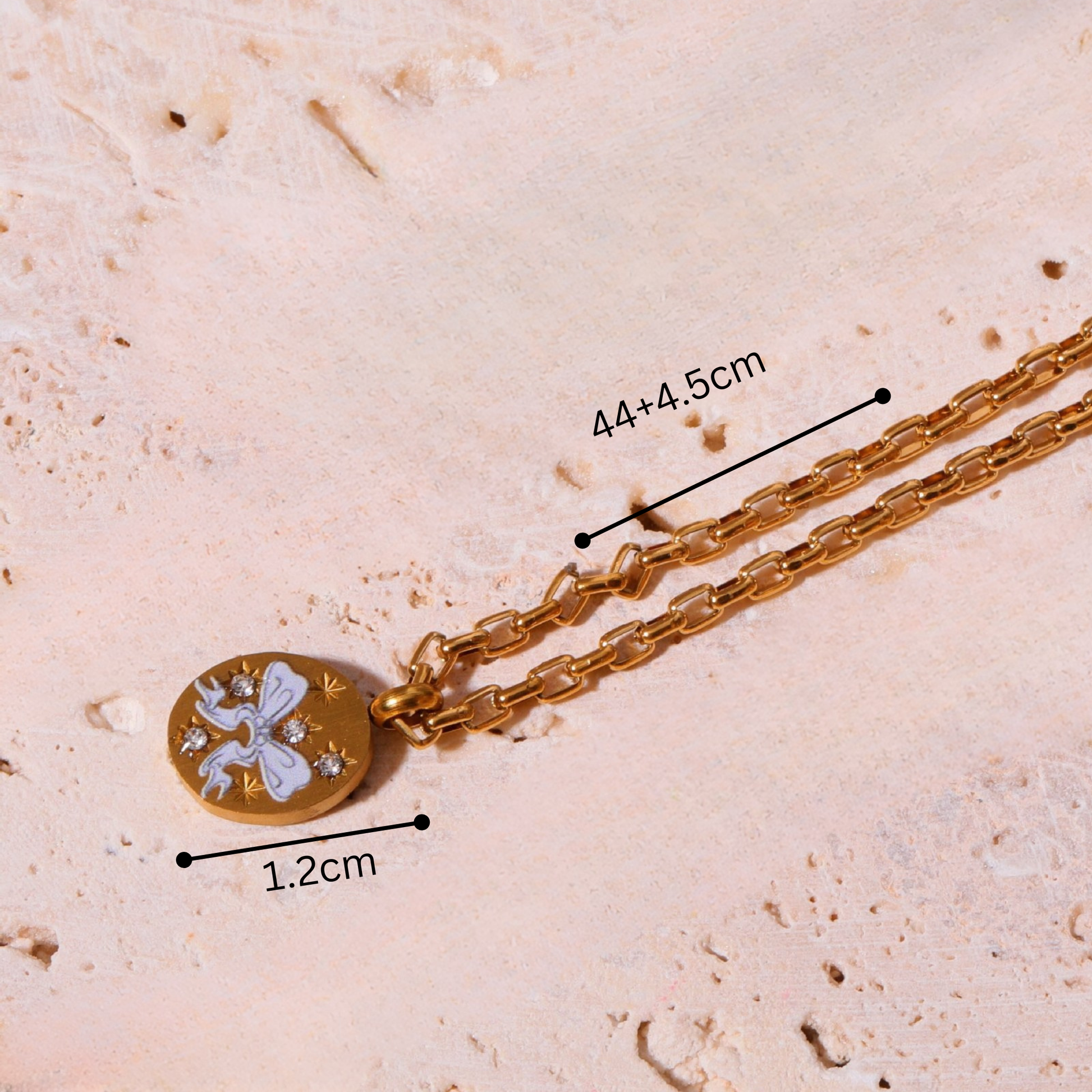 Gold necklace with a pendant on a textured beige surface, showing measurements.