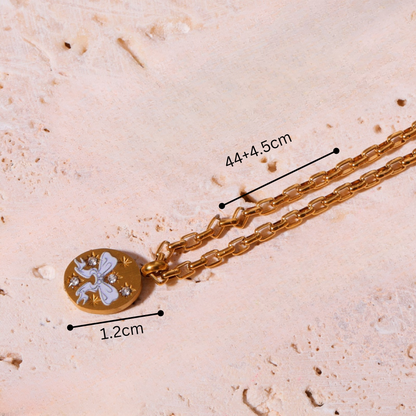 Gold necklace with a pendant on a textured beige surface, showing measurements.