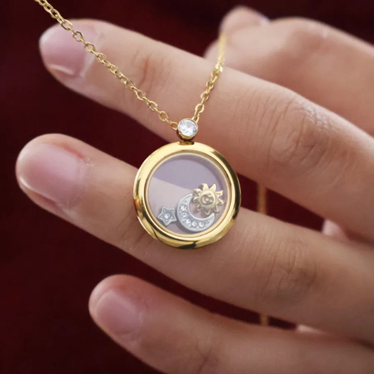 Gold necklace with a round pendant held by a hand against a red background