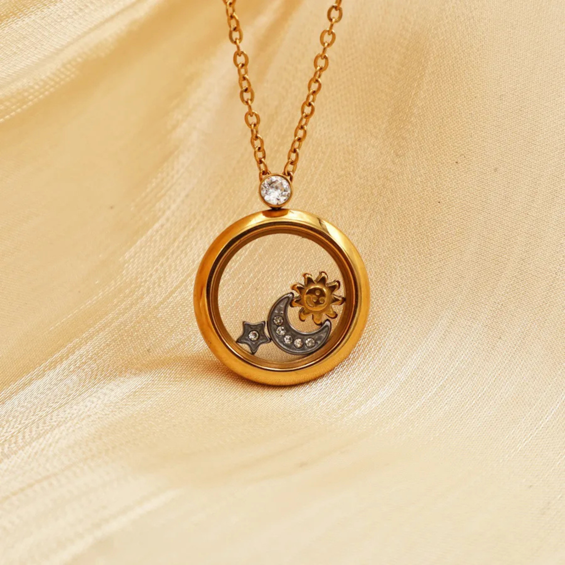 Gold necklace with a circular pendant featuring moon and sun designs on a beige fabric background