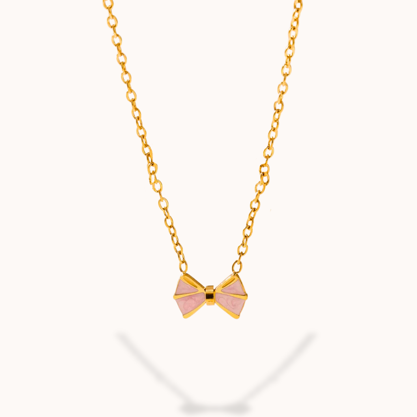 Gold necklace with a pink bow pendant on a white background