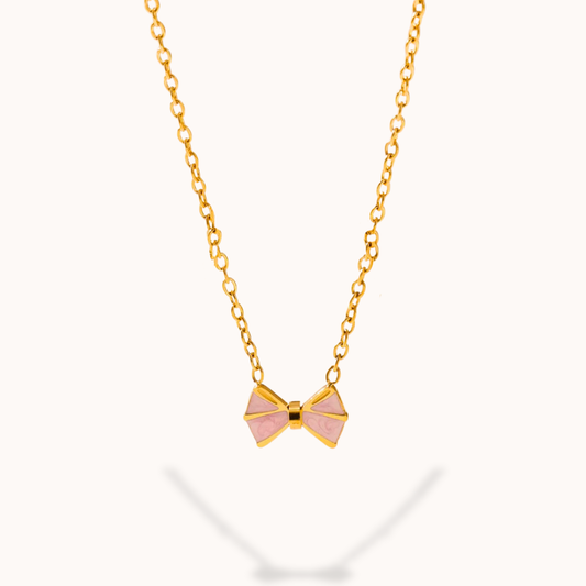 Gold necklace with a pink bow pendant on a white background